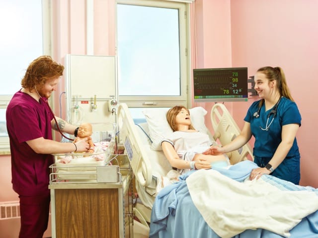 Deux étudiants pratiquent sur des mannequins les soins à prodiguer lors d'un accouchement