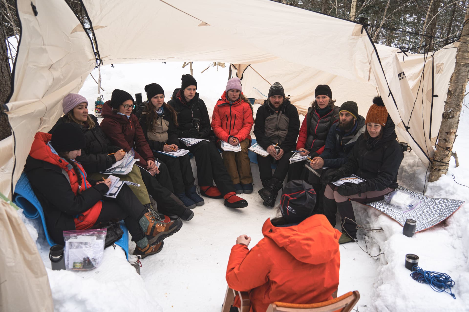 Un groupe de personnes en AEC Intervention par l'aventure et le plein air rassemblées sous une tente lors d'une expédition hivernale.