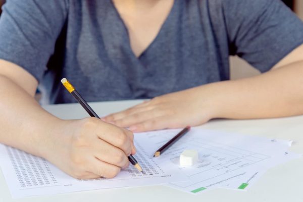 Students hand holding pencil writing selected choice on answer sheets and Mathematics question sheets. students testing doing examination. school exam